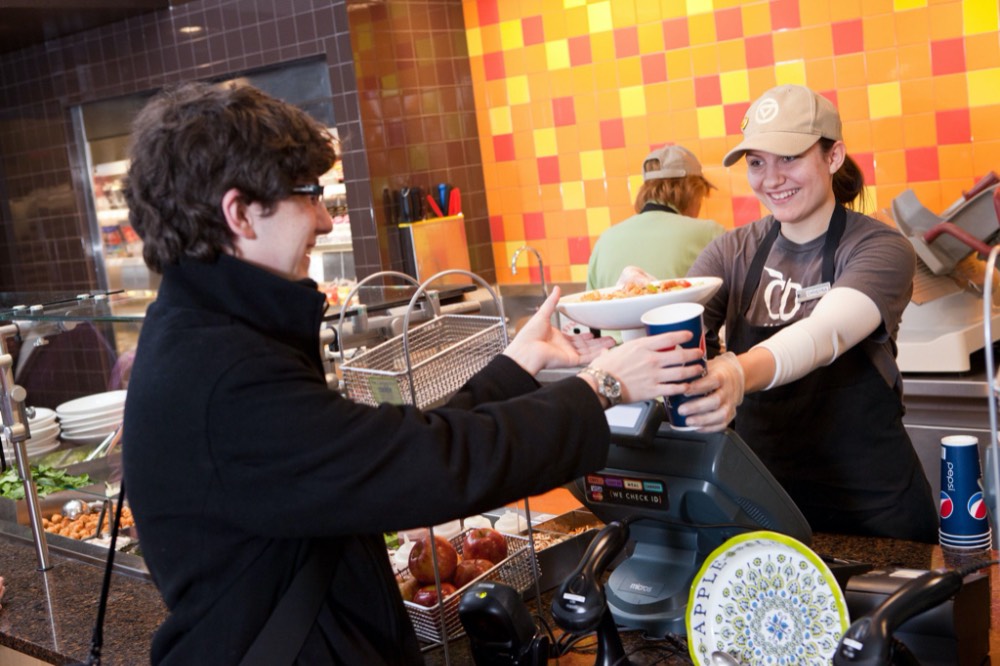 A student employee is handing a student a grain bowl and a fountain drink cup.